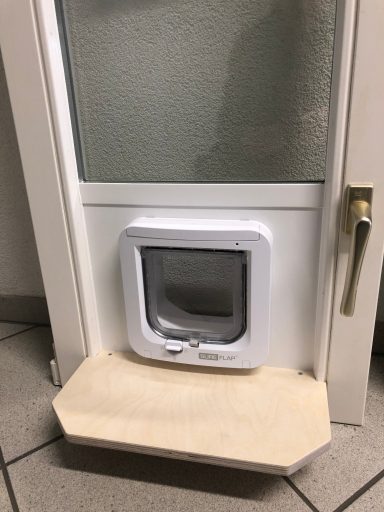 Katzentür mit transparentem Fenster in einer Tür, darunter ein Holzbrett.