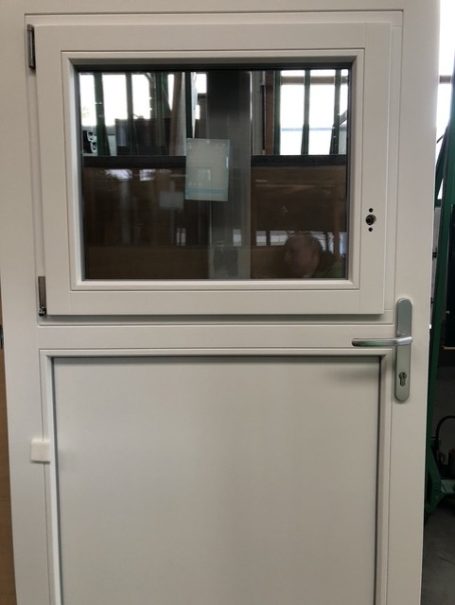 Weiße Tür mit Fenster und Griff, in einem Innenraum mit Arbeitsumgebung im Hintergrund.